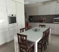 Modern kitchen with white cabinets, stainless steel appliances, a glass dining table with six wooden chairs, and a decorative bowl on the table.