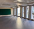 Empty room with grey carpeted floor, large windows, and a green wall panel.