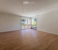 Empty room with wooden flooring, white walls, large windows, and a sliding glass door leading to a balcony.