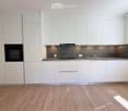 Modern kitchen with white cabinets, stainless steel sink, oven, and wooden flooring.