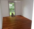 Empty room with wooden flooring, white walls, and a large window with a view of greenery outside.
