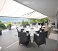 Balcony with a view of the city and mountains, featuring a round table, wicker chairs, a small stool, and a furry throw.