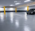 Underground parking area with a single car parked, concrete pillars, and fluorescent lighting.