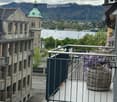 Balcony with metal railing, overlooking a scenic lake and cityscape with a prominent church dome in the background.