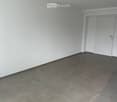Empty room with grey tiled floor and white walls, featuring a white door and electrical outlet visible on the wall.