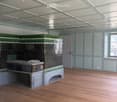 Empty room with wooden flooring, light blue walls, and a large green and black cabinet with intricate carvings. The ceiling features exposed beams and lighting fixtures.