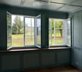 Empty room with wooden flooring, grey walls, large windows with open shutters, and a skylight ceiling.