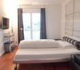 Modern bedroom with a large window and balcony access, featuring a bed, nightstand, lamp, and a TV on a stand.