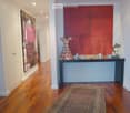 Elegant hallway with polished wooden flooring, recessed ceiling lights, a large red accent wall, and a decorative console table with a colorful sculpture and small items on top.