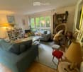 Bright living room with large windows, two sofas, coffee table, bookshelf, wicker chair, and decorative items.