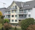 Modern multi-story residential building with multiple balconies, large windows, and a well-maintained garden area.