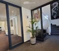 Modern hallway with carpeted floor, glass doors, potted plant, staircase, and artwork on walls.