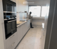 Modern kitchen with white cabinets, a built-in oven, and a sleek countertop, illuminated by a round ceiling light.