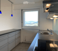 Modern kitchen with stainless steel sink, faucet, stove, and grey cabinets. Large window offers a scenic view.