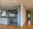 Modern kitchen with light grey cabinets, a central island, and built-in appliances. The space features wooden flooring, pendant lights, and a sleek design with open shelving.