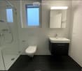 Modern bathroom with white tiles, black floor, glass-enclosed shower, toilet, sink with mirror, and built-in cabinet.
