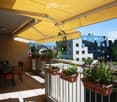 Balcony with a yellow retractable awning, several potted plants, and a small dining set with chairs and a table.