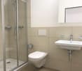 Modern bathroom with a toilet, sink, and glass-enclosed shower. Light-colored tiles and a sleek design.