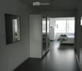 Modern, minimalist bedroom with dark flooring, large mirror, sliding wardrobe, and neatly made bed.