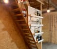A wooden staircase leads to a small bar area with shelves holding various bottles and glasses, illuminated by hanging lights.