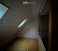 A narrow wooden hallway with slanted wooden ceiling and small skylight windows, leading to an open area.