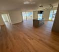 Open-plan space with wooden flooring, a kitchen island, large windows, and sliding glass doors leading to a balcony.