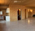 Open-plan space with exposed wooden ceiling and walls, featuring a small kitchen area with a refrigerator, sink, and cabinets, and a large open area with wooden walls and a polished concrete floor.