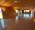Empty room with bare walls and polished concrete floor, wooden ceiling, large windows, and sliding glass door.