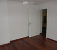 Empty room with white walls and wooden flooring, featuring an open door leading to another room.