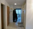 Corridor, white tiles, wooden door, rug, clothes on rack, light switch, bathroom door, glass door leading to a balcony with chairs and table