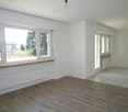 Empty room, white walls, wooden floor, large windows, heaters