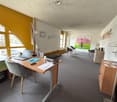 Office room with desk, chair, laptop, picture frames, cabinets, and large windows