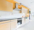 Modern kitchen with white cabinets, granite countertops, built-in oven and dishwasher, and yellow accent walls.