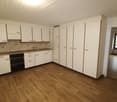 Empty kitchen with wooden floor, white cabinets, black appliances, sink, window.