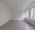 Empty room with white walls, wooden floors, large windows, heaters, no furniture