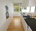 modern kitchen with white cabinets, wooden floor, black granite countertops, integrated oven and dishwasher