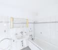 Clean and modern bathroom with white tiles, white bathtub, white sink, and white toilet