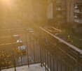 Outdoor balcony/terrace overlooking street with parked cars, trees, metal railing, table and potted plants