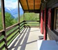wooden balcony, wooden railing, wooden floor, table, lamp, green grass, trees, mountains