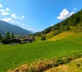large open grassy area with several houses, wooded hillsides, mountains in the distance