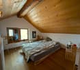 Spacious bedroom with wooden beamed ceiling, large windows, wooden floor, bed, and various furniture pieces