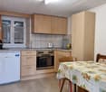 Fully equipped kitchen with wooden cabinets, tiled backsplash, stove, oven, dishwasher, and washing machine. Dining table with floral tablecloth in the corner.