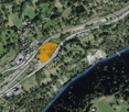 This is a map showing a rural area with a river running through it. There are several buildings and roads visible, as well as a large yellow-highlighted area that appears to be a parking lot or similar facility.
