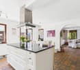 modern design with white cabinetry, granite countertops, large island, gas stove with hood, chandelier lighting, white walls, wooden floors, two windows with white curtains