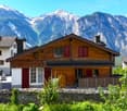 Alpine style wooden house, red shutters, mountains in the background