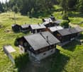 Cluster of traditional Swiss-style wooden chalets with slate roofs, surrounded by lush green meadows and pine forests in a mountainous landscape
