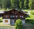 2-story wooden chalet-style house with a balcony, surrounded by lush green forest and meadows