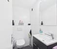 White tiled walls, black vanity unit with sink, toilet, shelves with decorative items