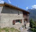 2-story stone and wood house with a slanted roof, wooden shutters, and a balcony overlooking a mountainous landscape
