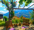 Wooden pergola with climbing vines, wooden benches, lush greenery and flowers, with a scenic mountain view in the background